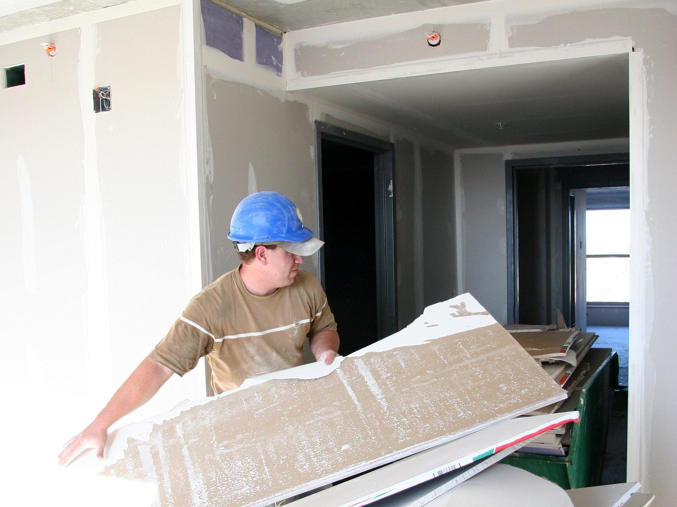 A construction worker pulling a tub of drywall waste through an unfinished building